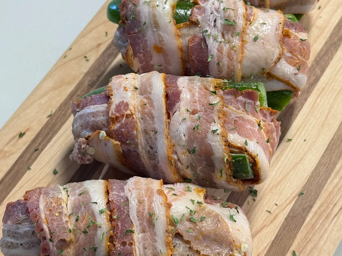 Bacon-wrapped jalapeño poppers sprinkled with herbs on a wooden board
