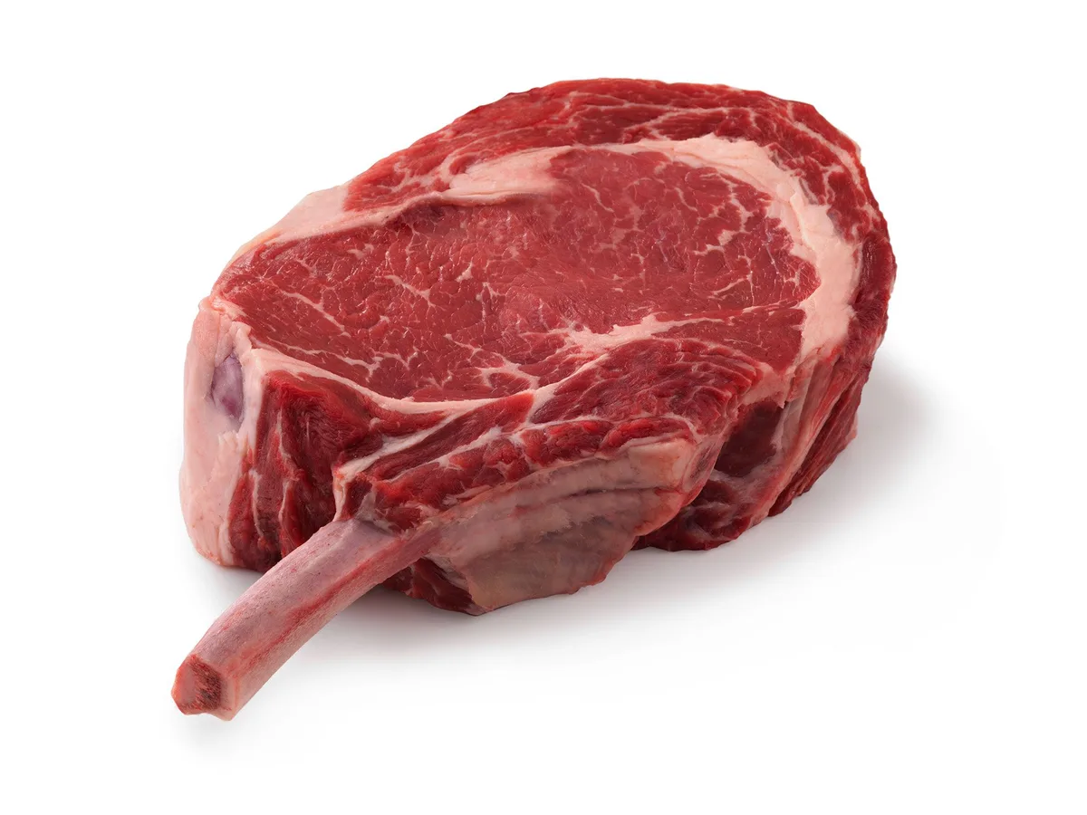 Raw bone-in cowboy cut ribeye steak on a white background