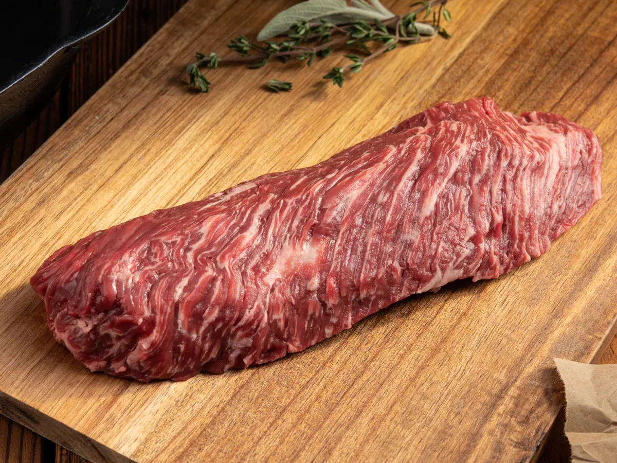 Raw beef hanger steak on a wooden cutting board with sage and thyme