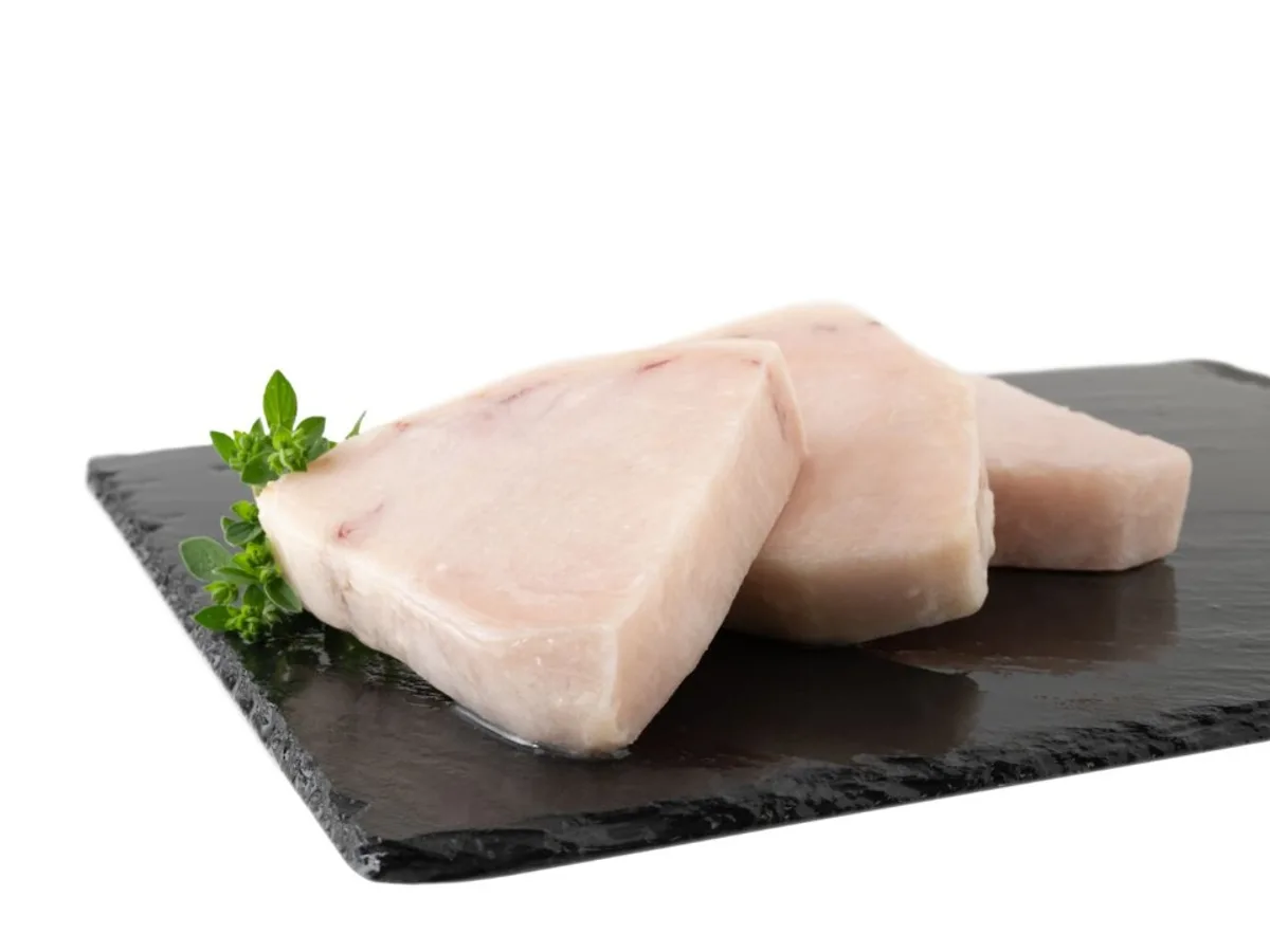 Three raw swordfish steaks on a slate board with fresh herbs