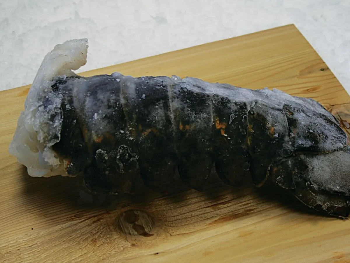 Frozen raw lobster tail in its shell on a wooden board